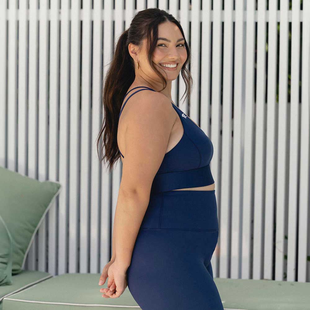A side profile of a smiling woman wearing navy activewear, showcasing the comfortable and supportive fit of the sports bra and leggings.