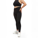 A woman wearing black leggings and a halter top, standing confidently with her hand on her hip, showing off the sleek design of the activewear.