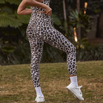 A side view of a woman in leopard-print leggings, highlighting the flattering fit of the activewear as she confidently adjusts her waistband, mid-action.