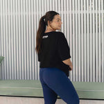 A woman wearing a black oversized tee, showcasing the back view of the fitness apparel. The "Active Elite" logo is visible on the upper back, while the fit is relaxed and comfortable.