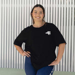A front view of a smiling woman wearing a black oversized tee and navy leggings. She stands confidently, with her hand on her hip, exuding a relaxed yet sporty vibe in her fitness attire.