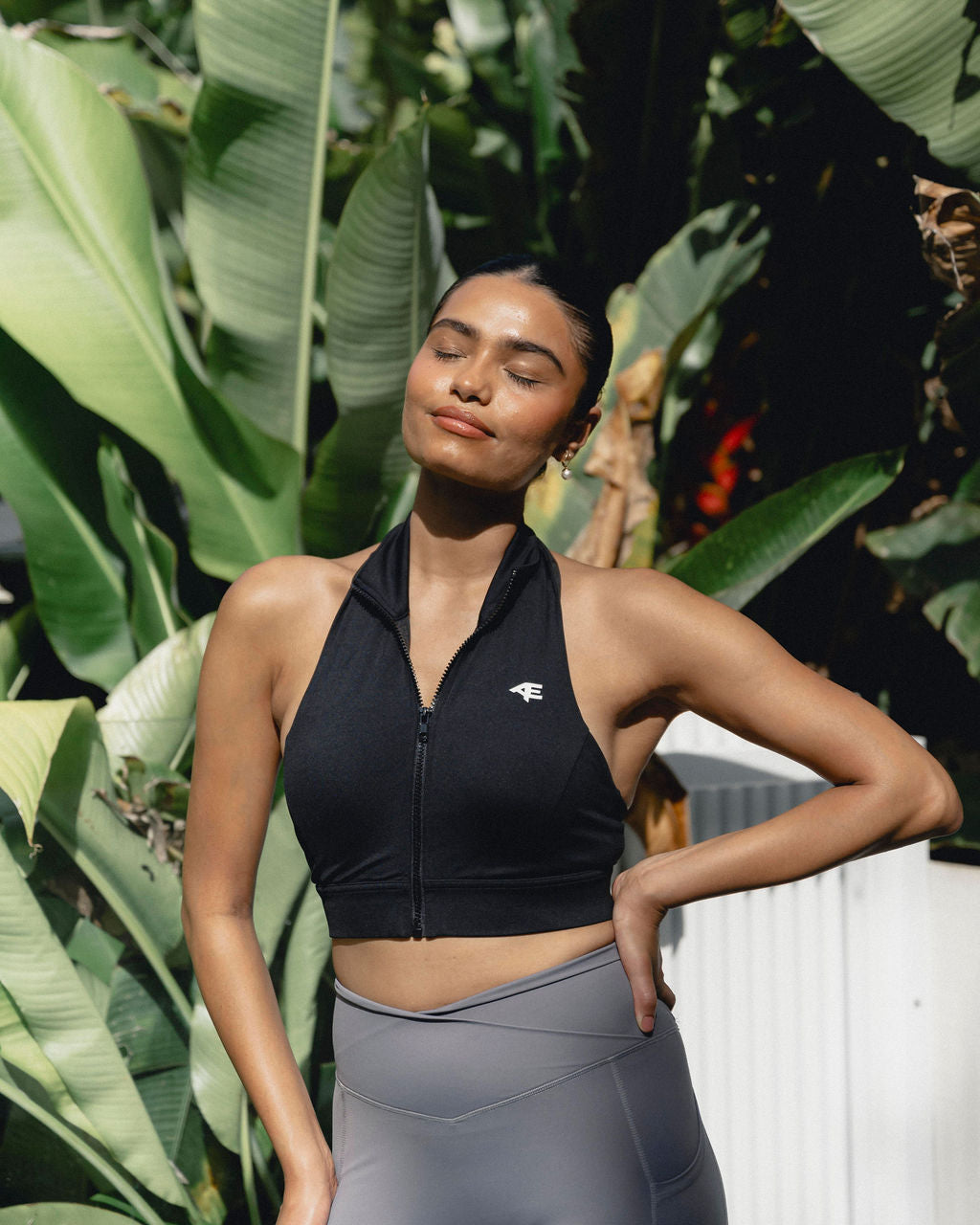 A woman in a halter-style activewear top standing in a garden setting, radiating confidence and peace.