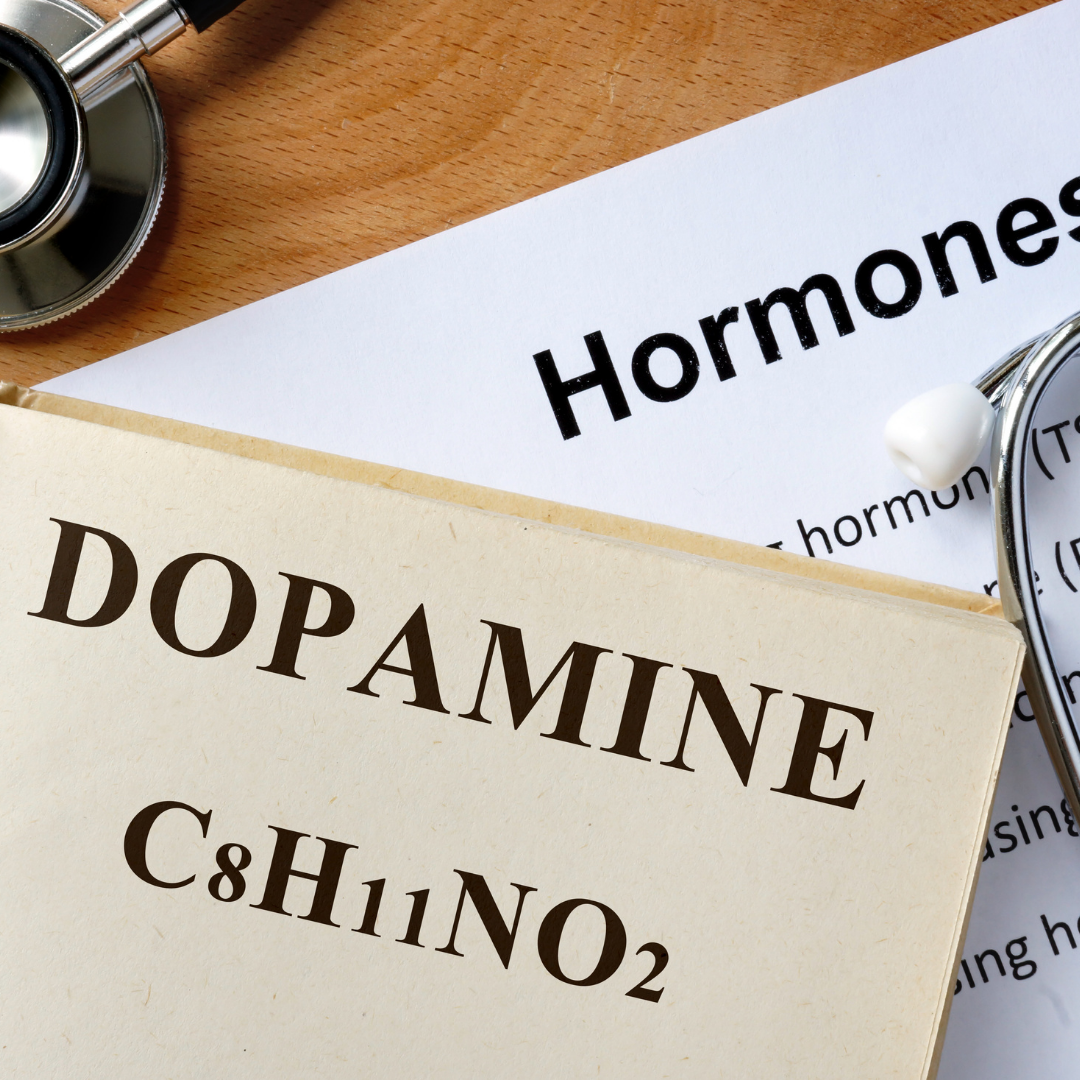 A notepad with "Dopamine" written on it alongside a pair of eyeglasses, suggesting the importance of understanding the role of hormones in well-being.