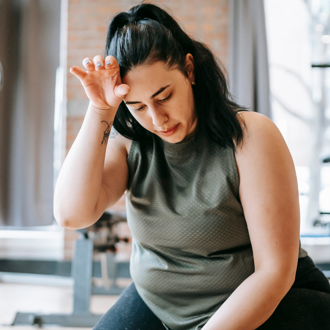 A woman in a grey tank top resting her head in her hand, looking thoughtful, possibly after a workout, representing moments of reflection and perseverance.
