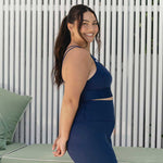 A side profile of a smiling woman wearing navy activewear, showcasing the comfortable and supportive fit of the sports bra and leggings.