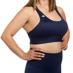 A close-up view of a woman in a navy sports bra, highlighting the detailed design, supportive structure, and empowering pose.