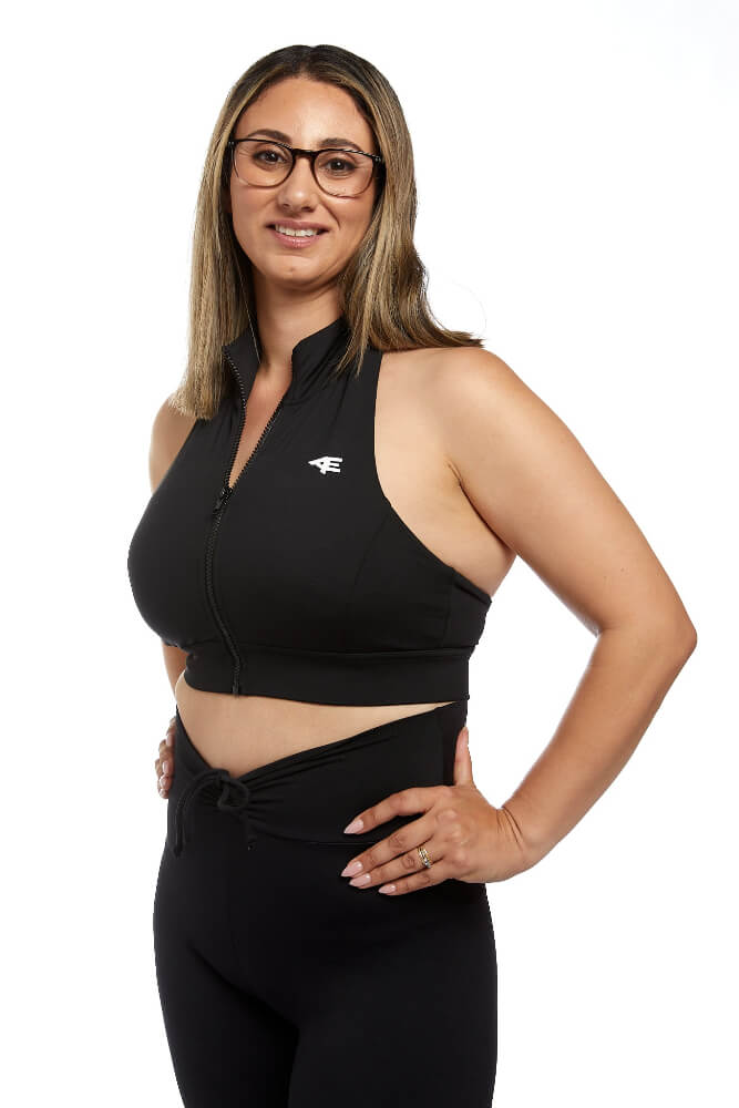 view of woman smiling at camera wearing black activewear halter sports crop. Hands on hips. Slightly turned to the side