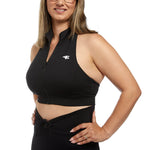view of woman smiling at camera wearing black activewear halter sports crop. Hands on hips. Slightly turned to the side