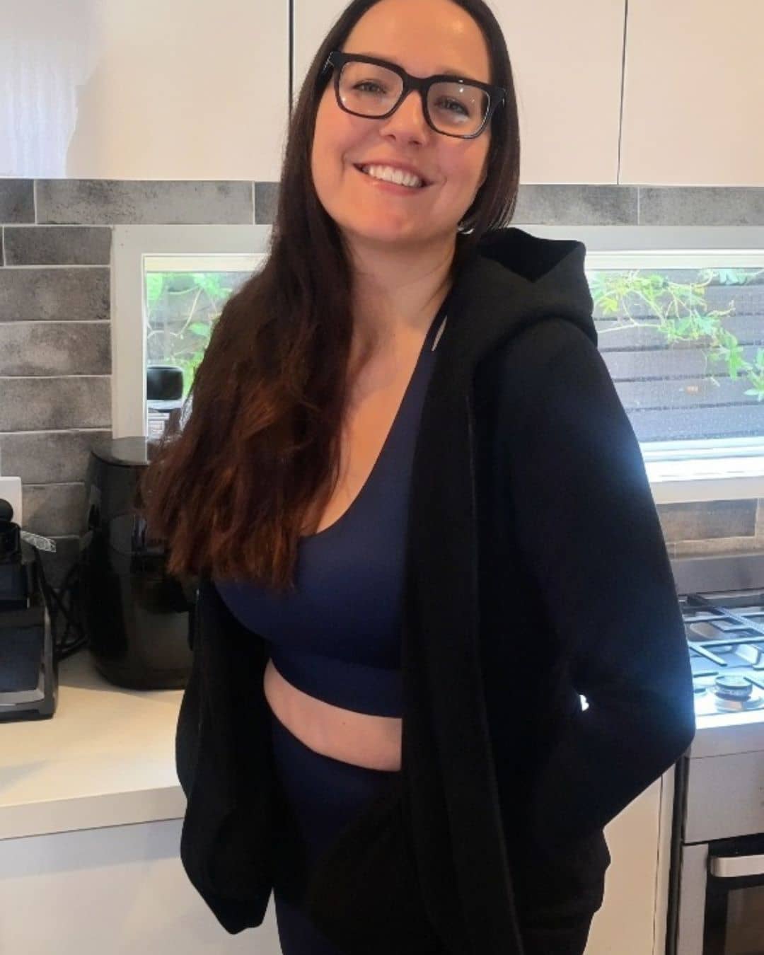 Woman wearing a black hoodie and blue top in a kitchen